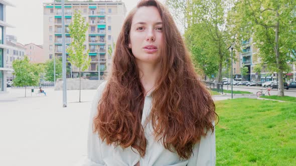 Woman with long hair standing in city, staring at camera