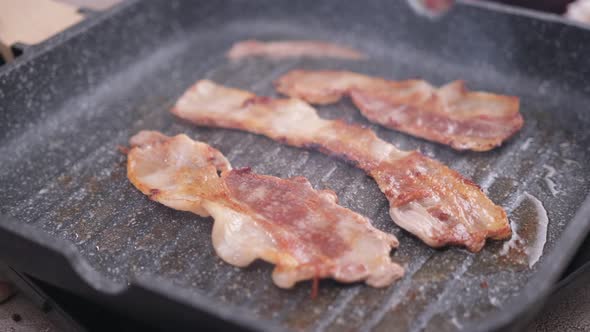 Cooking Pieces of Flavorful Sliced Organic Bacon Fried in Grill Pan