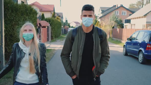 Multiethnic Man and Woman in Medical Masks Walking Down the Street in Housing Estate