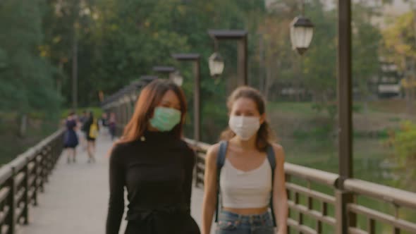 Portrait of Two Young Women in Love Wearing Protective Face Medical Mask Standing in Park at Sunset