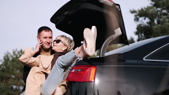 Husband and Wife Sit on Car Trunk and Cuddle in Nature