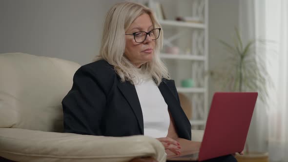 Portrait of Focused Psychologist Sitting with Laptop on Armchair Checking Time on Watch