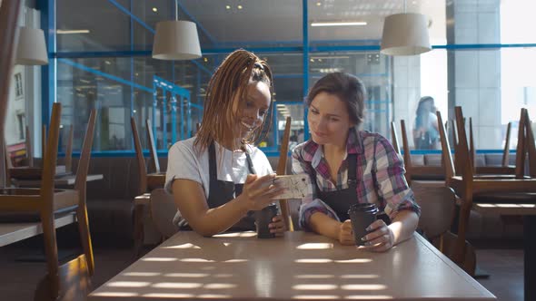 Portrait of Two Young Happy Diverse Saleswomen with Coffee and Phone at Coffee Shop or Cafe