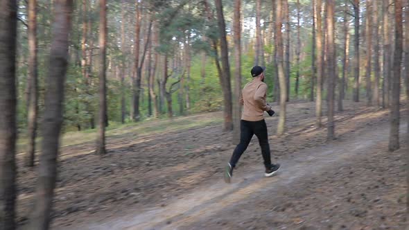 Man in black cap with camera in hands running in the forest