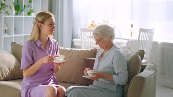 Young girl and elderly mother talking with cups of tea