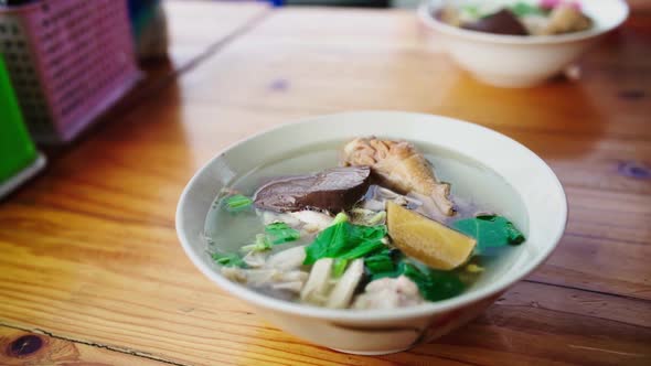 A full bowl of hot delicious Thai chicken soup with rice noodles, sprouts and greens in an outdoor s