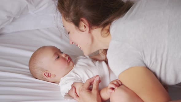Loving Young Mommy Hugging Soothing Adorable Sweet Baby Girl Lying in Bed