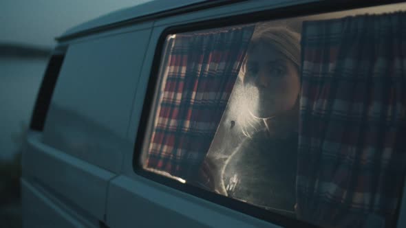 Woman Looking through Window of Camper Van in Evening