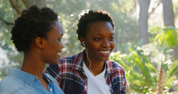 Twin sisters listening music on earphones in the park 4k