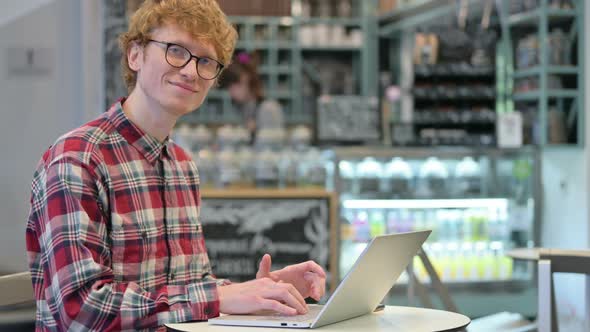 Young Redhead Man with Laptop Smiling at the Camera 