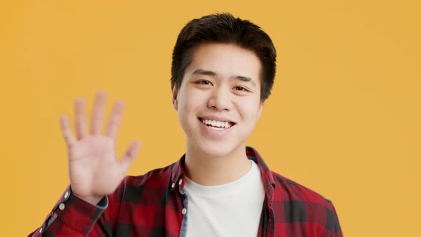 Joyful Asian Man Waving Hello Posing Standing On Yellow Background