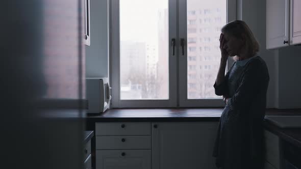 Depressed Lonely Elderly Woman Leaning on the Kitchen Cupboard