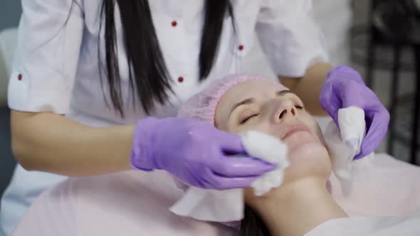 A beautician in gloves holds sanitary napkins in her both hands and cleans the skin