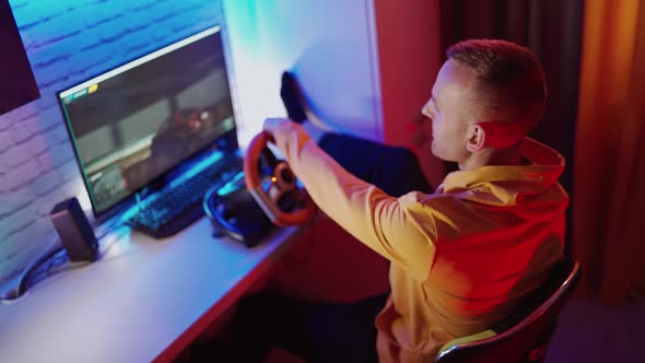 Man paying car simulator. Handsome man playing with steering wheel in video game at home