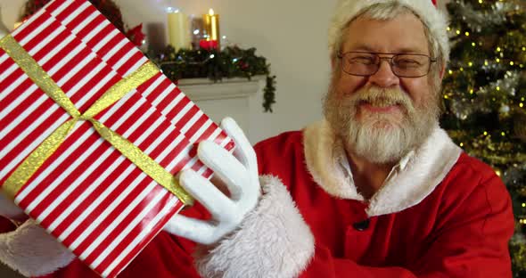 Portrait of santa claus holding gift box with finger on lips