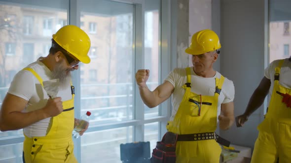 Cheering Diverse Construction Workers Dancing and Laughing in Renovating Apartment