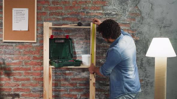 Black Man Measures Wooden Shelving Unit with Roller Tape