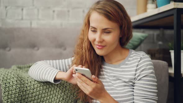 Happy Young Woman Is Holding Smartphone Touching Screen and Smiling Checking Social Media Account or