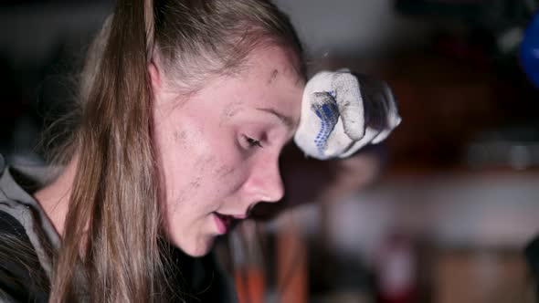 Close-up of a young woman with a dirty face who repairs motorcycle equipment