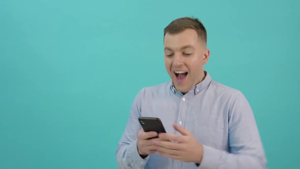 A Man in a Blue Shirt is Corresponding on a Smartphone and Expresses Great Joy and Surprise