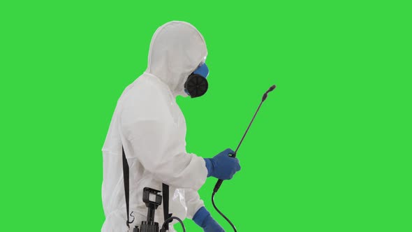 Man in a Hazmat Suit Walking and Spraing with a Disinfectant on a Green Screen, Chroma Key.
