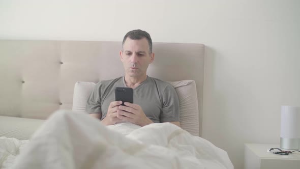Male siting in bed on his smartphone gets a dramatic message