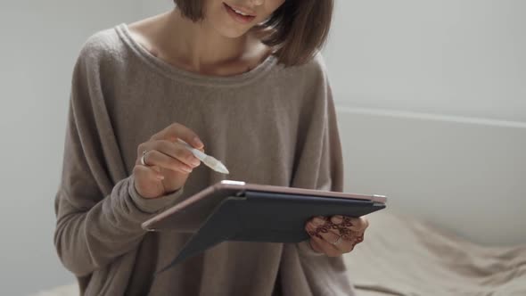 Young Smiling Woman Is Using Stylus Pen and a Tablet in Her Bedroom in Daytime