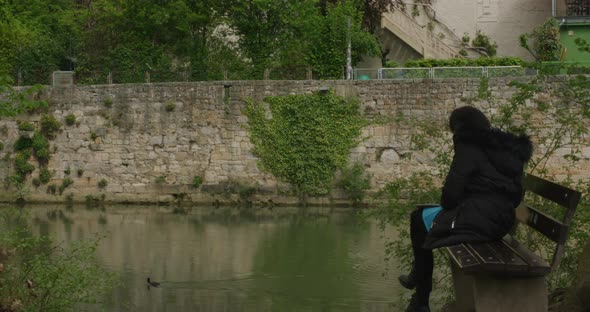 Stylish woman on bench calmly watching duck passing by in Tubingen downtown river in Balvaria, Germa