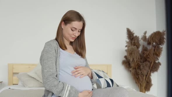 Pregnant Woman in Home Clothes Sitting on a Double Bed