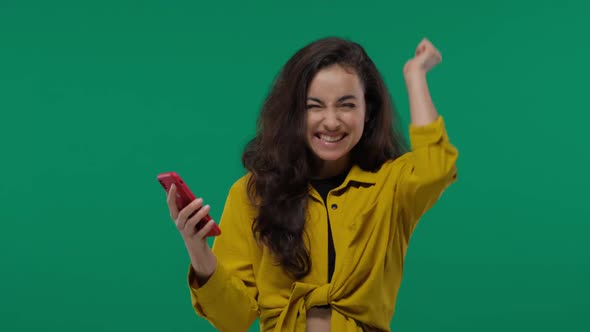 Happy Brunette Woman Rejoices While Holding Smartphone and Looking at the Camera on Green Screen