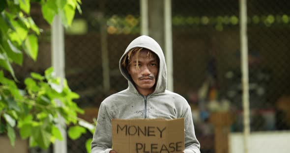Homeless man holding money please label and looking at camera.