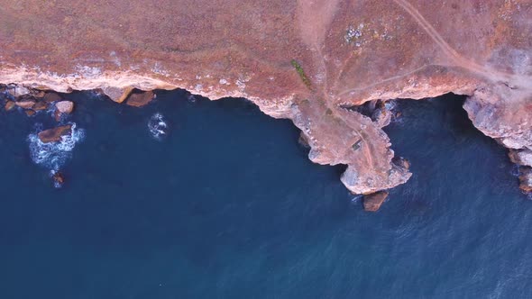 Top down aerial view of waves splash against rocky seashore, background. Flight over high cliffs of