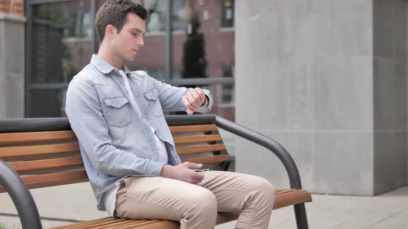 Waiting Young Man Sitting on Bench and Checking Time