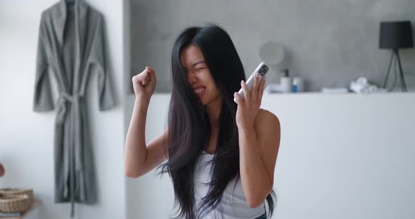 Happy Young Asian Woman Rejoices at Message While Using Smartphone in Bathtub