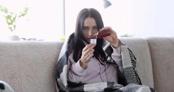 Cold Woman Pours Cough Syrup While Sitting on Couch