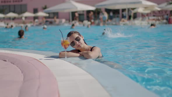 Miss with Sunglasses Drinks a Cocktail While in the Pool