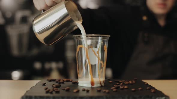 A Barista Pouring Milk Into a Plastic Cup with Caramel on the Sides
