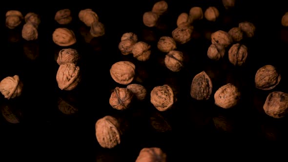 Walnuts in the shell falling on the black reflective surface in slow motion.