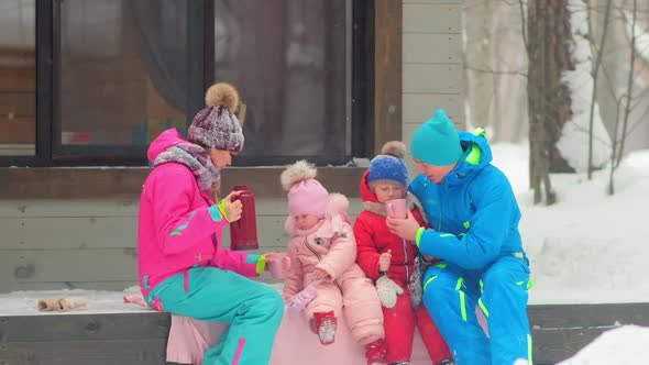 Parents and Children Drink Tea Sitting on Building Porch