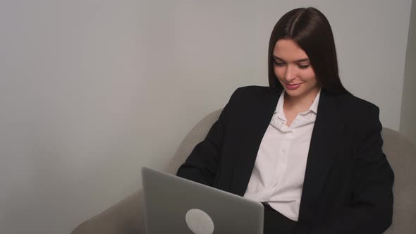 Smiling Young Businesswoman Sitting on Couch Using Laptop Looking at Screen Typing Message Lady