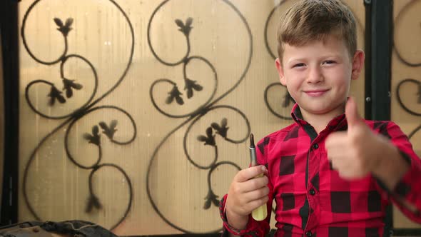 Little Boy Holds a Screwdriver in His Hand Looks at the Camera and Turns It