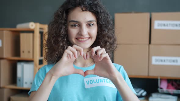 Slow Motion Portrait of Happy Young Woman Volunteer Making Heart Hand Gesture and Smiling in Charity