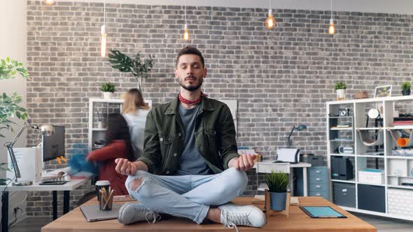 Time-lapse of Young Man Relaxing in Lotus Position on Desk in Office