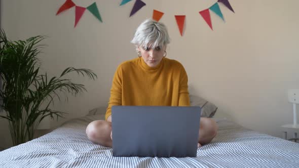 Woman sitting on the bed working with laptop