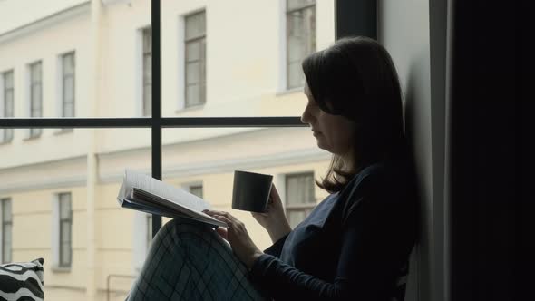 Female with Cup of Tea Reading Book on Windowsill