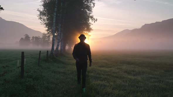 Man In Silhouette Walking In Misty Meadow From Sunrise