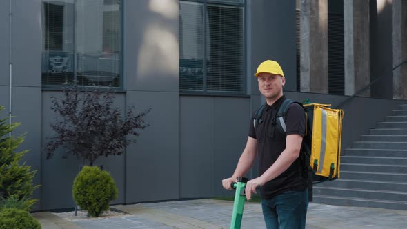 Delivery Man with Yellow Backpack Rides a Electric Scooter Through the City with