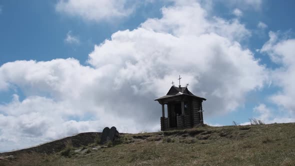 Small Old Wooden Chapel on Top of Mountain on Background Moving Clouds in Sky.
