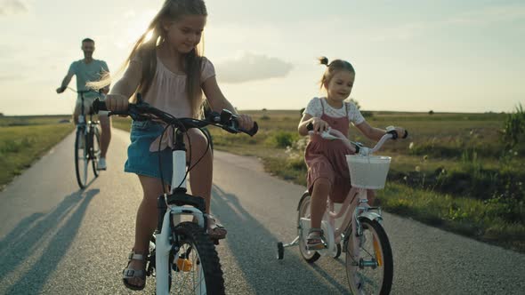 Caucasian family of two elementary age girls on foreground and parents in the background riding bike