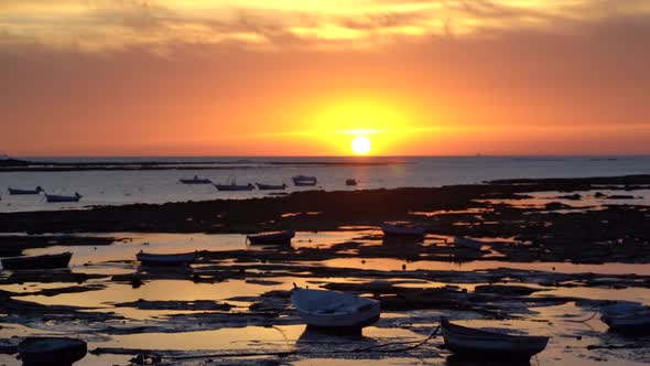 Slow tilt up over small fishing boats parked at low tide during sunset